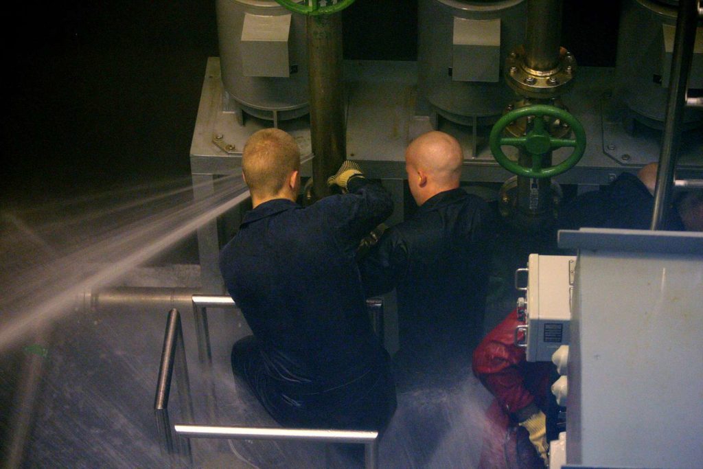 A team of midshipmen works to patch a ruptured pipe in the Trident Training Facility damage control wet trainer